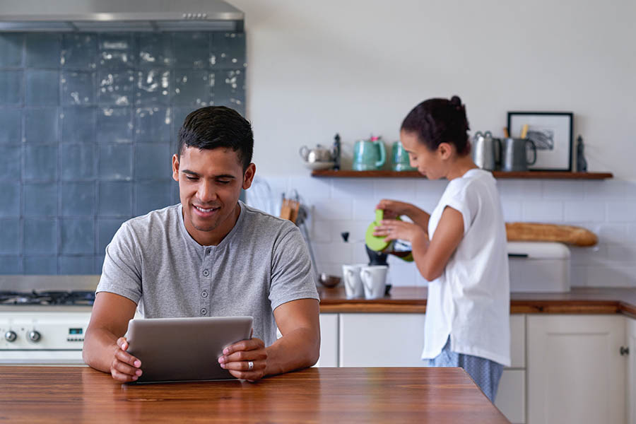Blog - Couple Relaxing in Kitchen, Wife Pouring Coffee While Husband Reads Tablet at the Kitchen Island